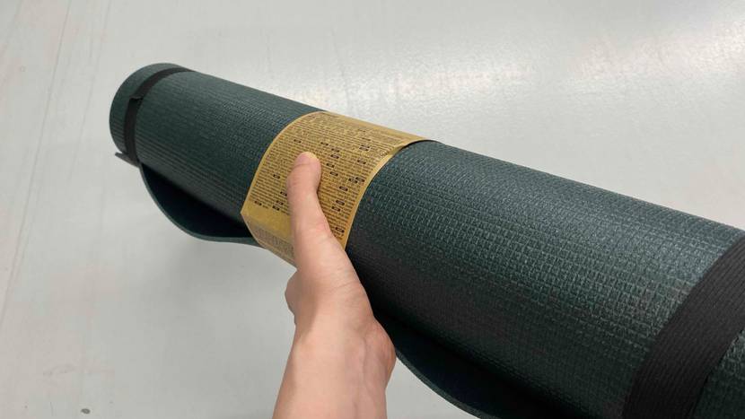 Yogamatte getestet: Eine Hand hält eine gerollte Matte vor eine helle Wand.