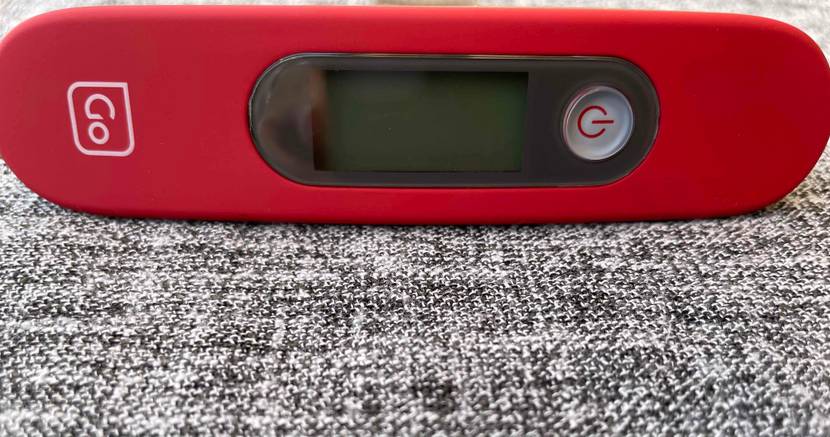 Rote batteriebetriebene Go-Kofferwaage im Test auf meliertem Hintergrund.