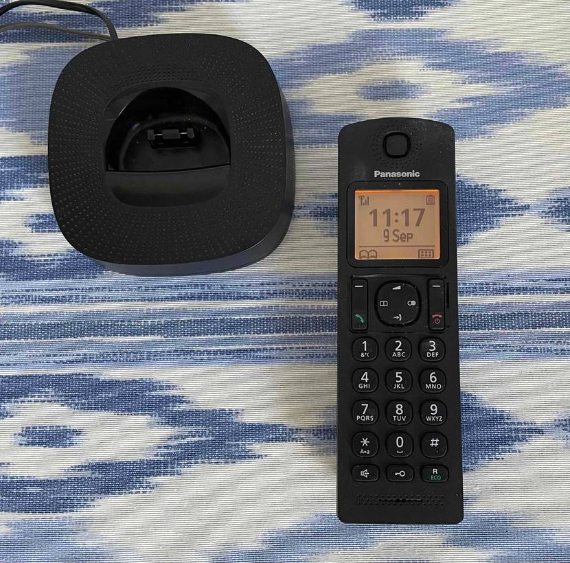 Getestetes schnurloses Telefon von Panasonic mit Blick auf Display und Wahl-Tasten liegt neben Lade-Basis.
