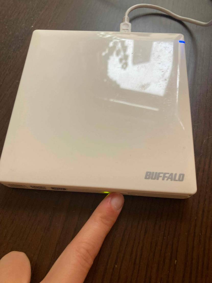 Eine Hand drückt einen Knopf am getesteten externen DVD-Laufwerk.