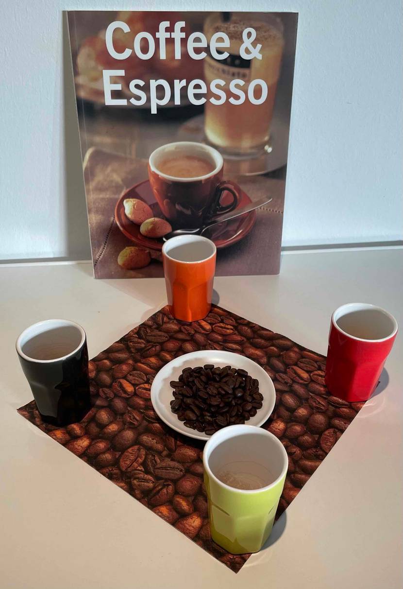 Espressobohnen getestet: Ein Buch lehnt an der Wand im Vordergrund vier Espressotassen um einen Teller mit Bohnen