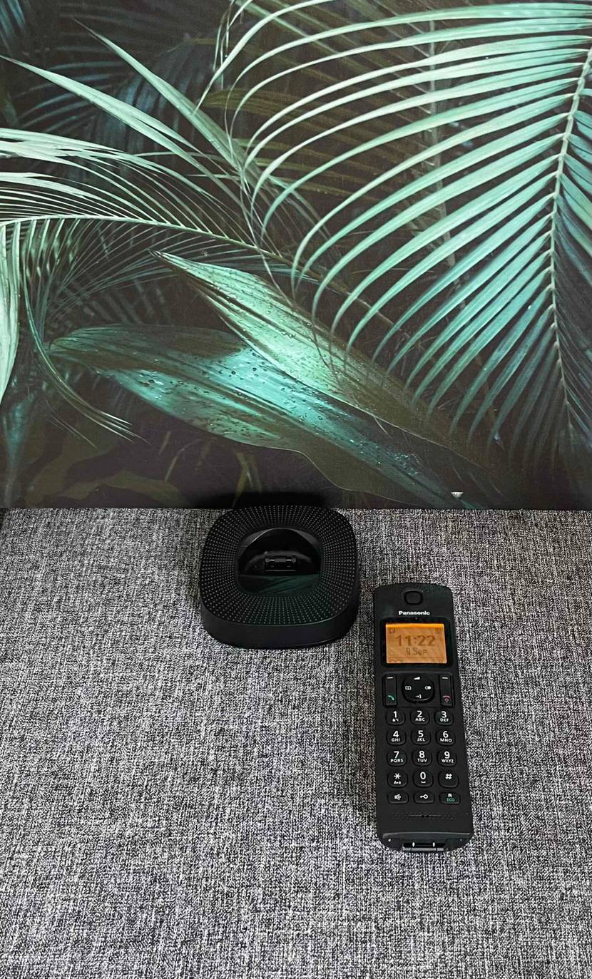 Liegendes getestetes schnurloses Telefon von Panasonic gibt Blick auf LCD-Anzeige und Wahl-Tasten frei, und die Ladastation steht link daneben.