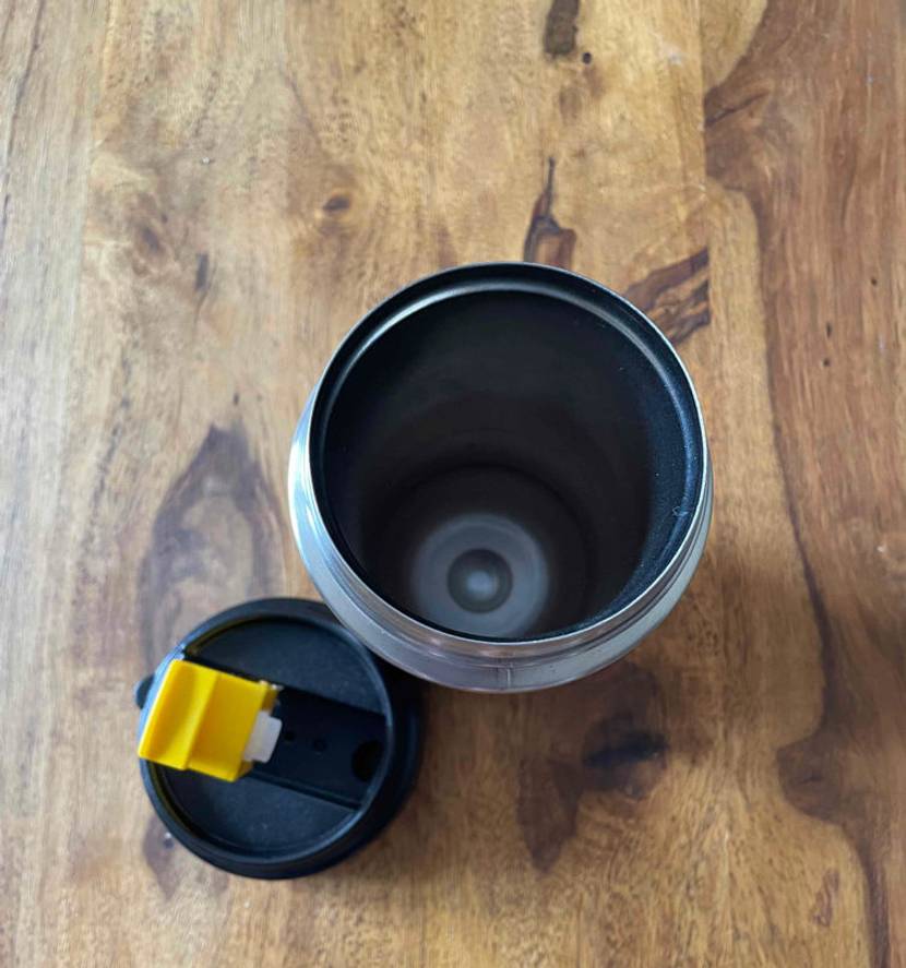 Thermobecher im Test: Ein geöfnneter Edelstahlbecher steht auf einem Holzboden, während der Deckel daneben liegt.