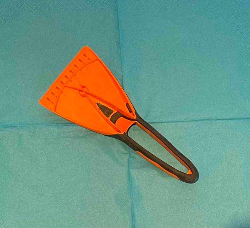 Oranger Eiskratzer im Test inklusive schwarz gummiertem Handgriff liegt auf türkisfarbenem Papier.