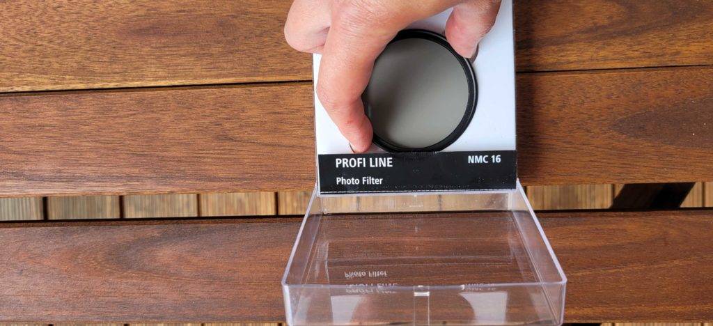 Polfilter im Test: Geöffnete Verpackung des Hama Polfilters liegt auf einem Holzuntergrund, während eine Hand den Polfilter selbst auf der Verpackung platziert.