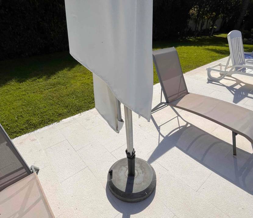 Sonnenschirm im Test: eingeklappter Sonnenschirm in einem Garten stehend mit dunklem Standfuß.