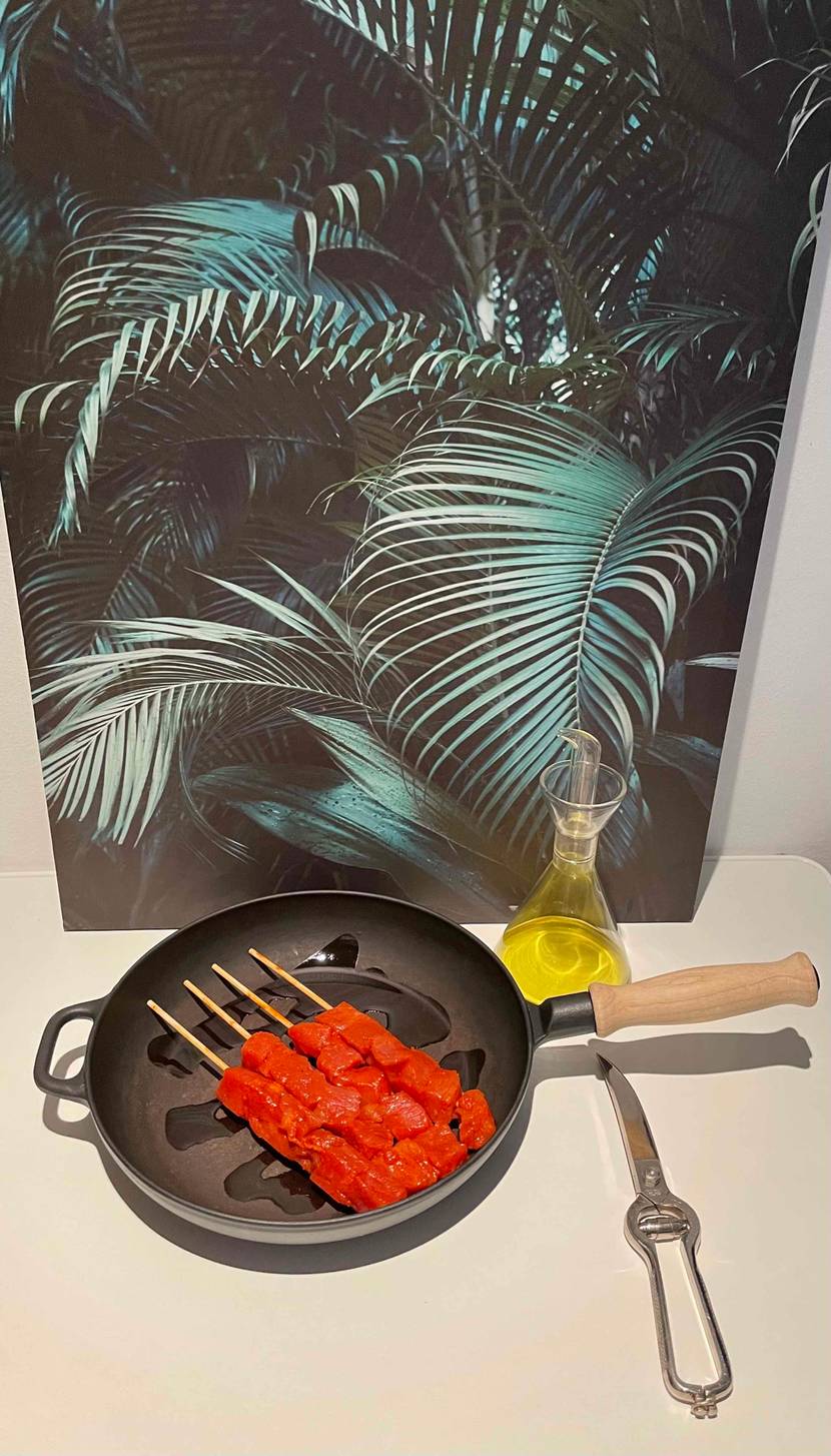 Getestete Geflügelschere liegt geschlossen auf Tisch neben Pfanne mit Fleischstücken und Ölkaraffe.