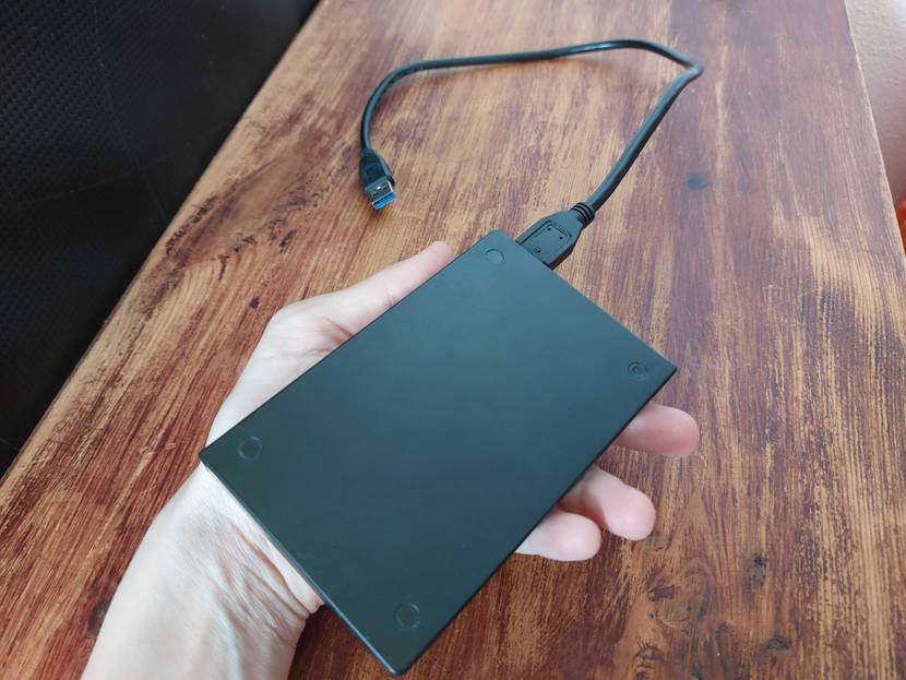 SSD Festplatte getestet: Eine Hand hält eine SSD mit Kabel vor eine Holzfläche