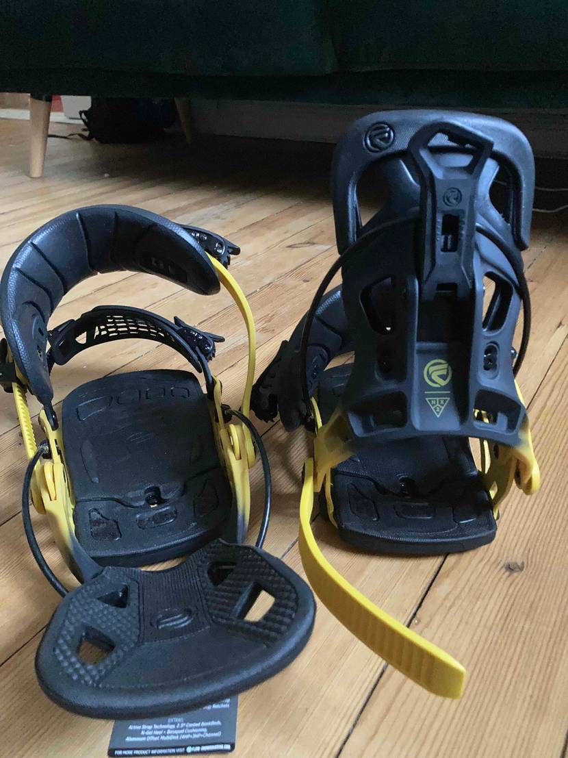 Auf einem Holzboden stehen zwei getestete Snowboard-Bindungen.