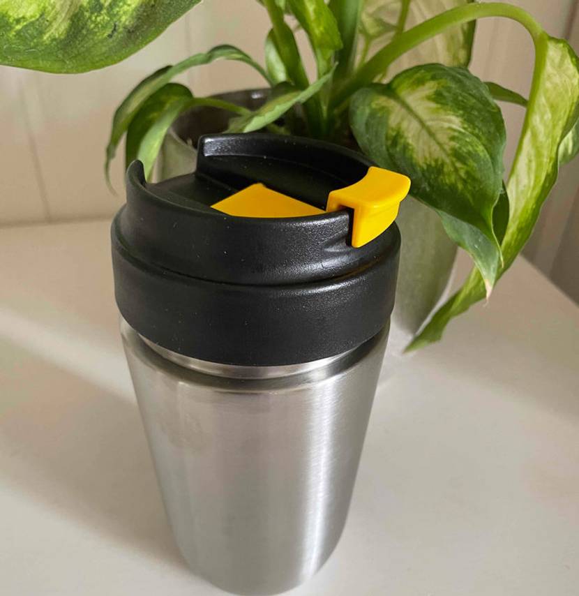 Getesteter Thermobecher aus Edelstahl steht auf einem weißen Tisch vor einer Zimmerpflanze.