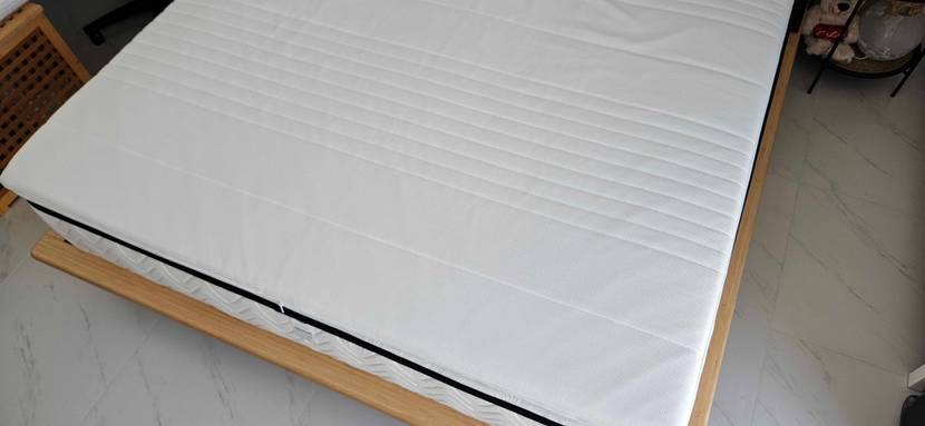 Topper-180x200-Test: ein weißer Topper in einem geschlossenen Zustand liegend auf einem Bett.