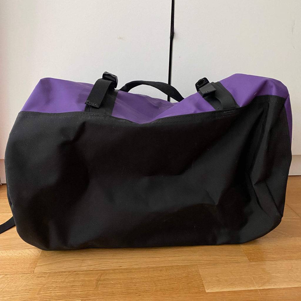 Getestete Reisetasche in schwarz-lila liegt auf der Seite auf einem Holzboden, sodass man den Boden sehen kann.