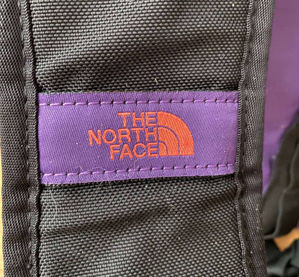 Reisetasche-Test: Detailaufnahme des Logos der Marke The North Face in Lila und Orange auf einem schwarzen Hurt der Reisetasche.