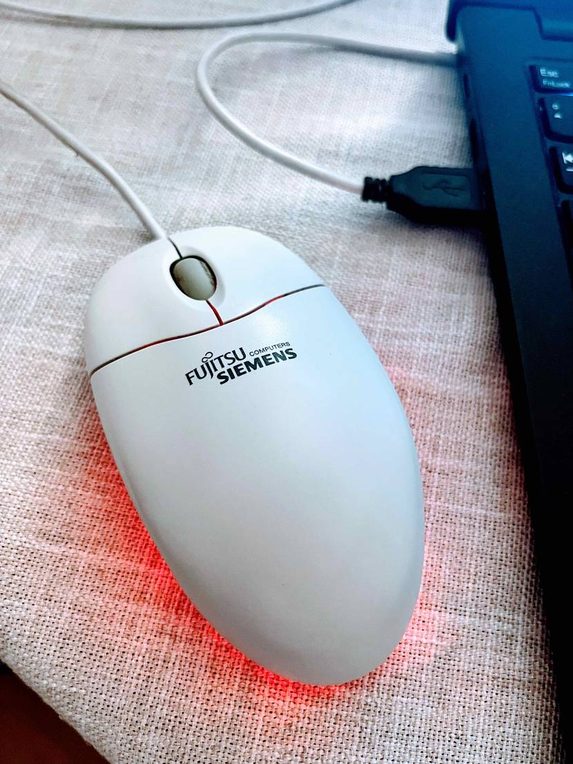 PC-Maus getestet: Eine Maus von oben neben einem Laptop, die Unterseite leuchtet rot.