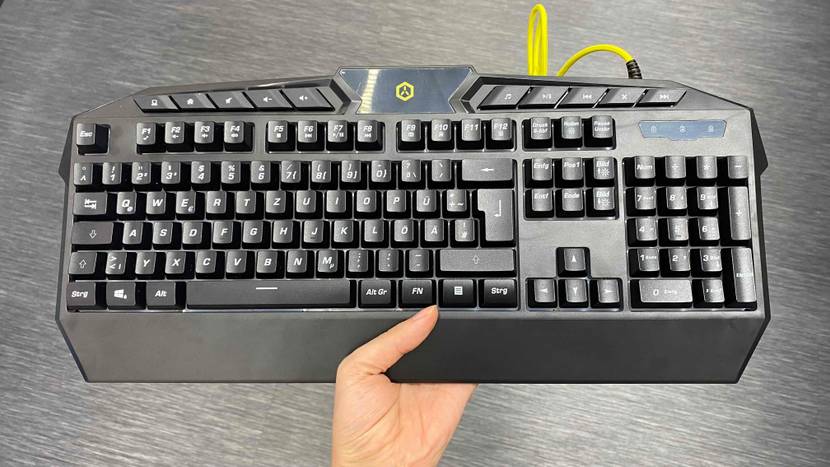 Getestete Gaming-Tastatur wird mit Hand über einem grauen Tisch gehalten