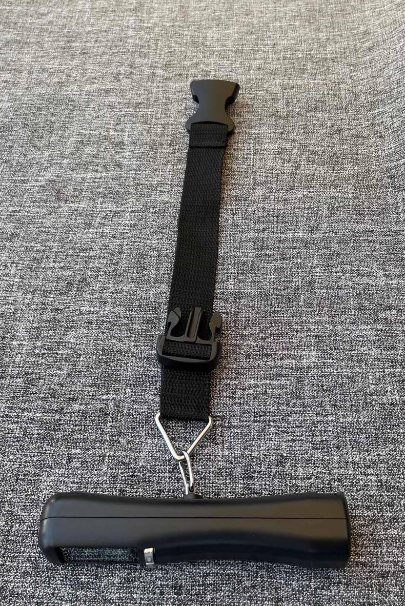 Schwarze getestete Kofferwaage inklusive Halteband mit Clip-Verschluss.