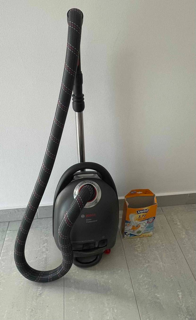 Staubsauger mit Beutel im Test: Ein Sauger neben einer Packung Beutel vor heller Wand