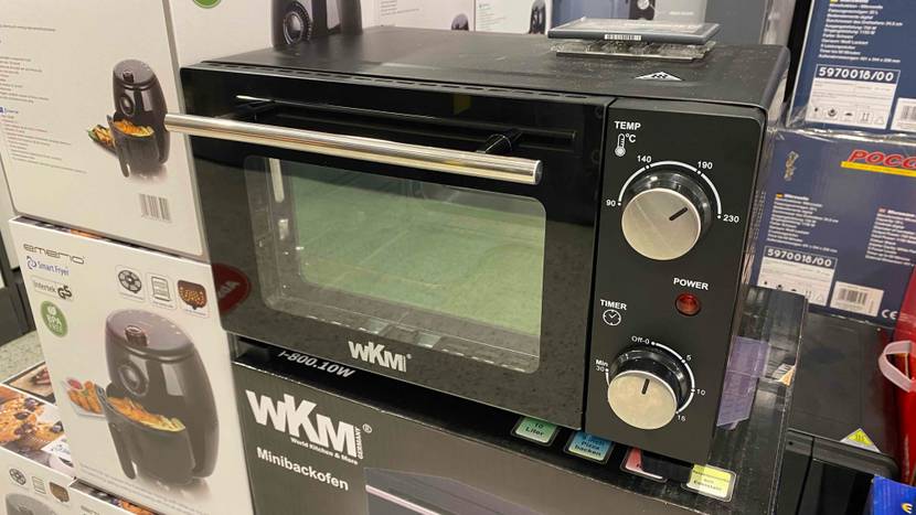 Ein Minibackofen von schräg vorne auf und neben verschiedenen Kartons.