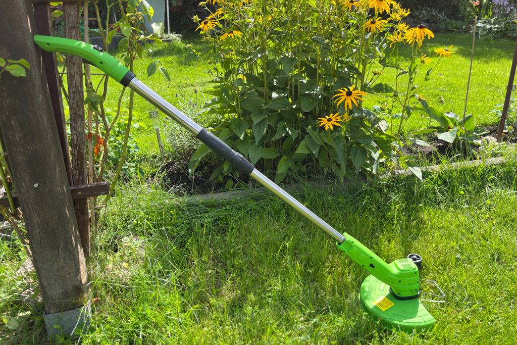 Akku-Rasentrimmer im Garten an einem Holzbalken lehnend