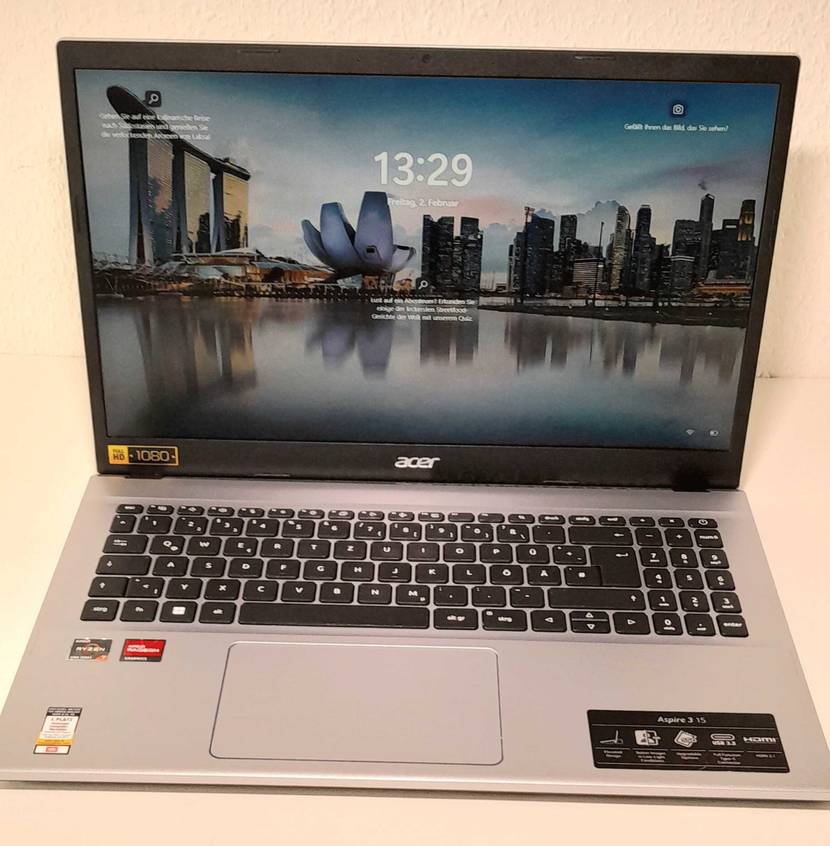 Laptop-15-Zoll-Test: ein eingeschalteter hellgrauer Laptop mit schwarzer Tastatur ist von vorn, mit hochgeklapptem Bildschirm vor einer weißen Fläche ausgestellt.