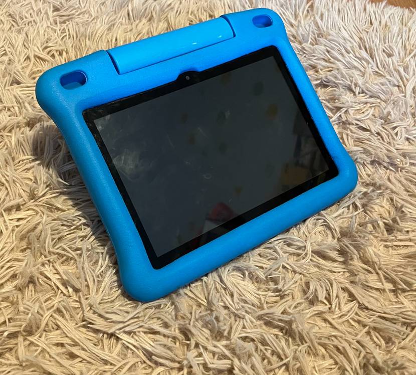 Ein getestetes Kinder Tablet mit einer blauen Hülle leicht erhöht auf einer beigen Stofffläche.