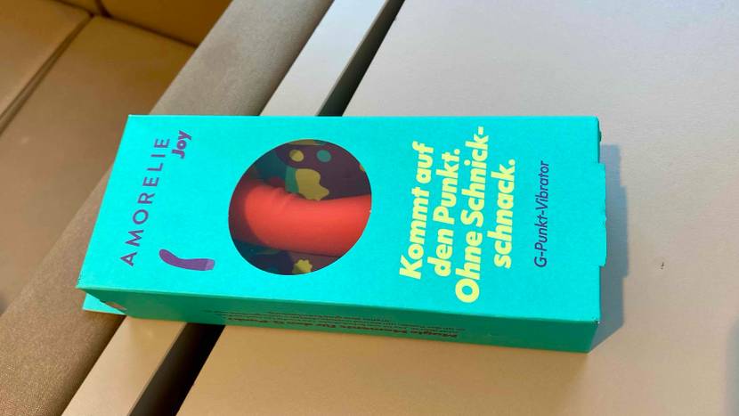 Im Test: ein Vibrator liegt in seiner grün-türkis farbigen Verpackung mit Sichtfenster auf einer hellen Fläche.