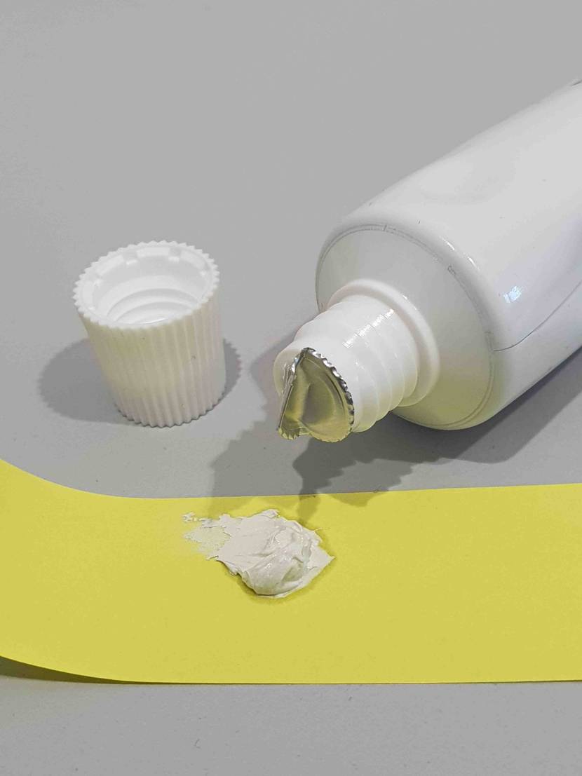Ein Klecks getestete Wärmeleitpaste liegt vor einer offenen Tube auf einer gelben Fläche.