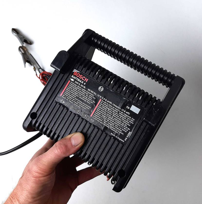 Eine Hand hält das getestete Autobatterie-Ladegerät mit der Rückseite nach vorne.
