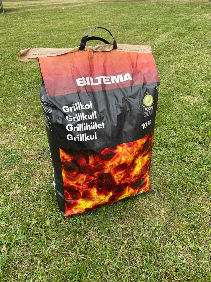 Geschlossener Sack Grillkohle auf einer Wiese.