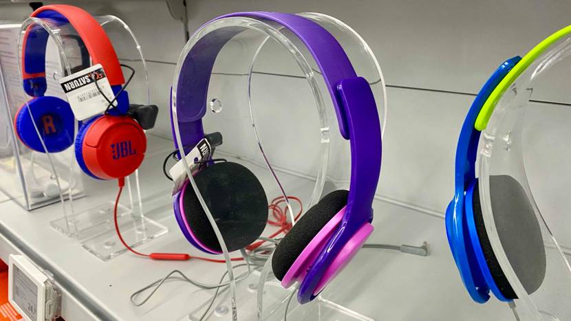 Ein getesteter Bluetooth Kopfhörer für Kinder auf einem transparenten Ständer zwischen anderen Geräten in einem Verkaufsregal.
