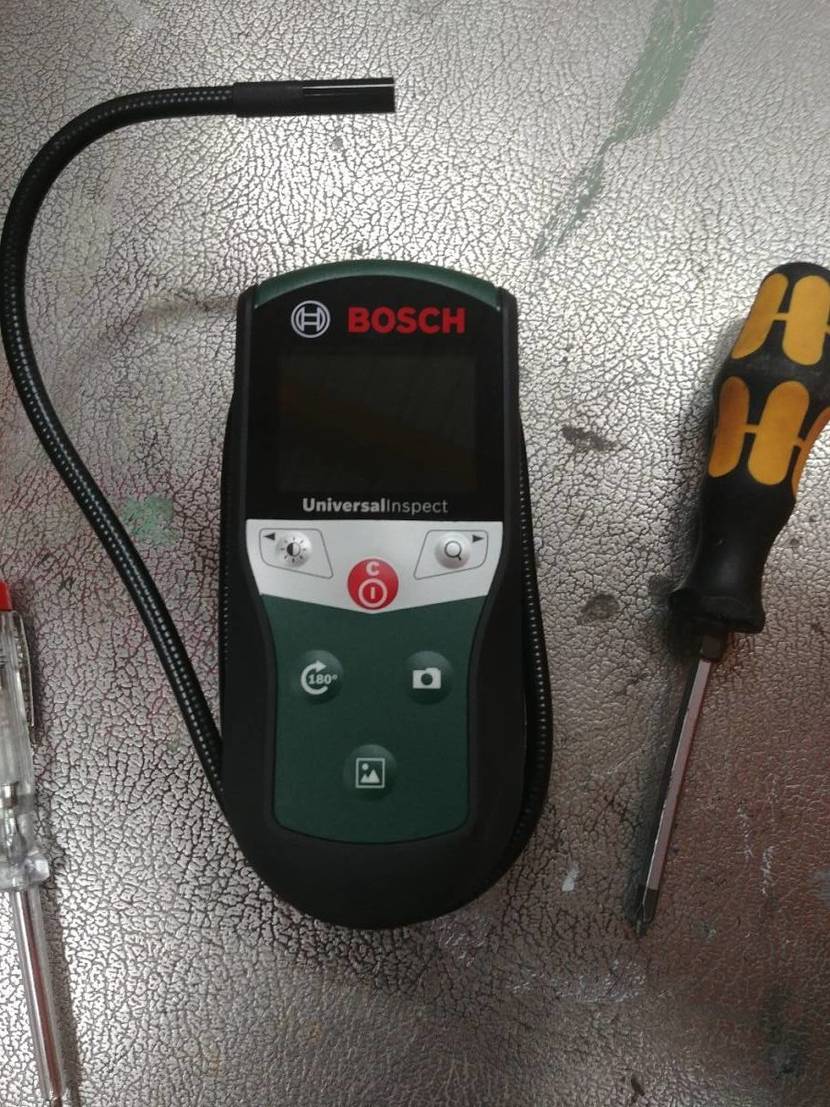 Endoskop-Kamera im Test: das Modell 603687000 der Marke Bosch auf einem silberfarbigen Untergrund zwischen zwei Schraubendrehern, mit Blick auf den beweglichen Schlauch mit Kamera.
