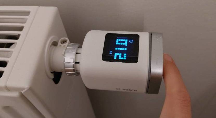 Smart-Home-Thermostate im Test: Finger an weißen Bosch-Smart-Home-Thermostat II inklusive LCD-Anzeige, an einem Heizkörper montiert.