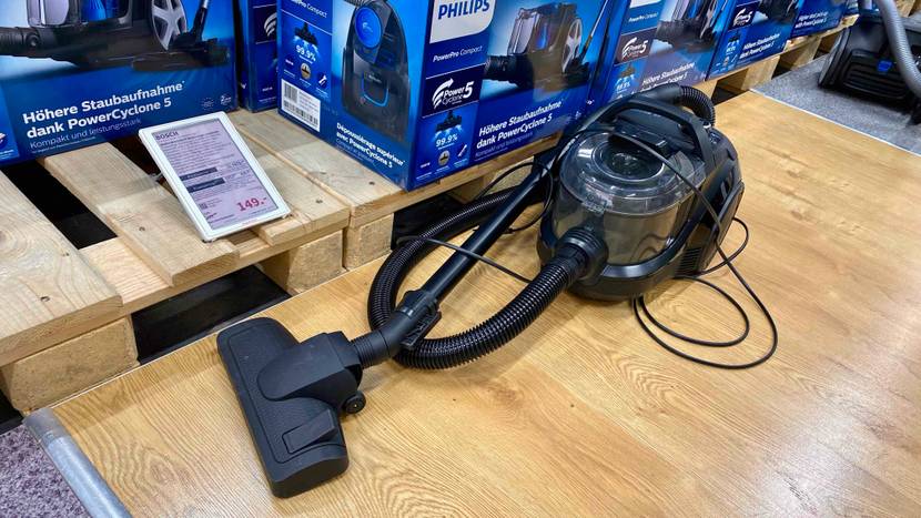 Im Test: Ein Bosch-Staubsauger mit eingewickeltem Kabel auf einer Holzfläche vor mehreren verpackten Geräten inklusive Preisangabe.