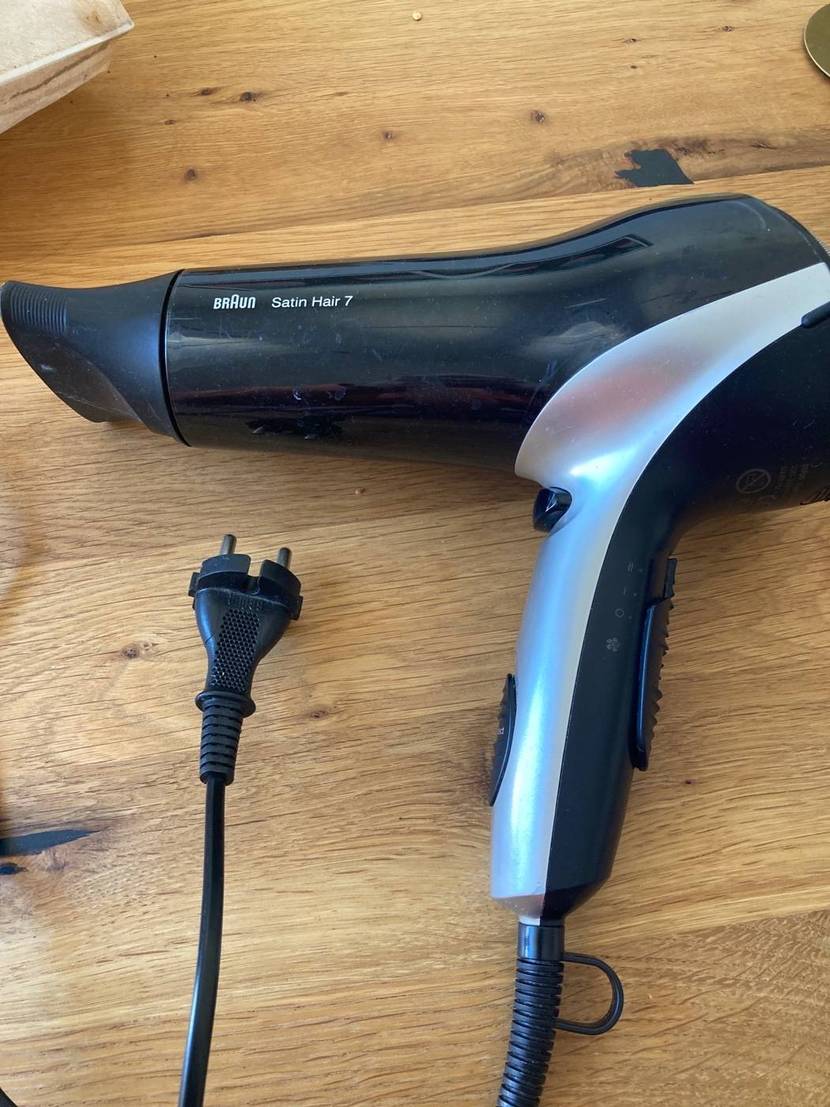 Ionen-Haartrockner-Test: Nahaufnahme eines Modells Braun Satin Hair 7 in Schwarz-Silber-Design inklusive Stecker-Kabel auf Holzuntergrund.