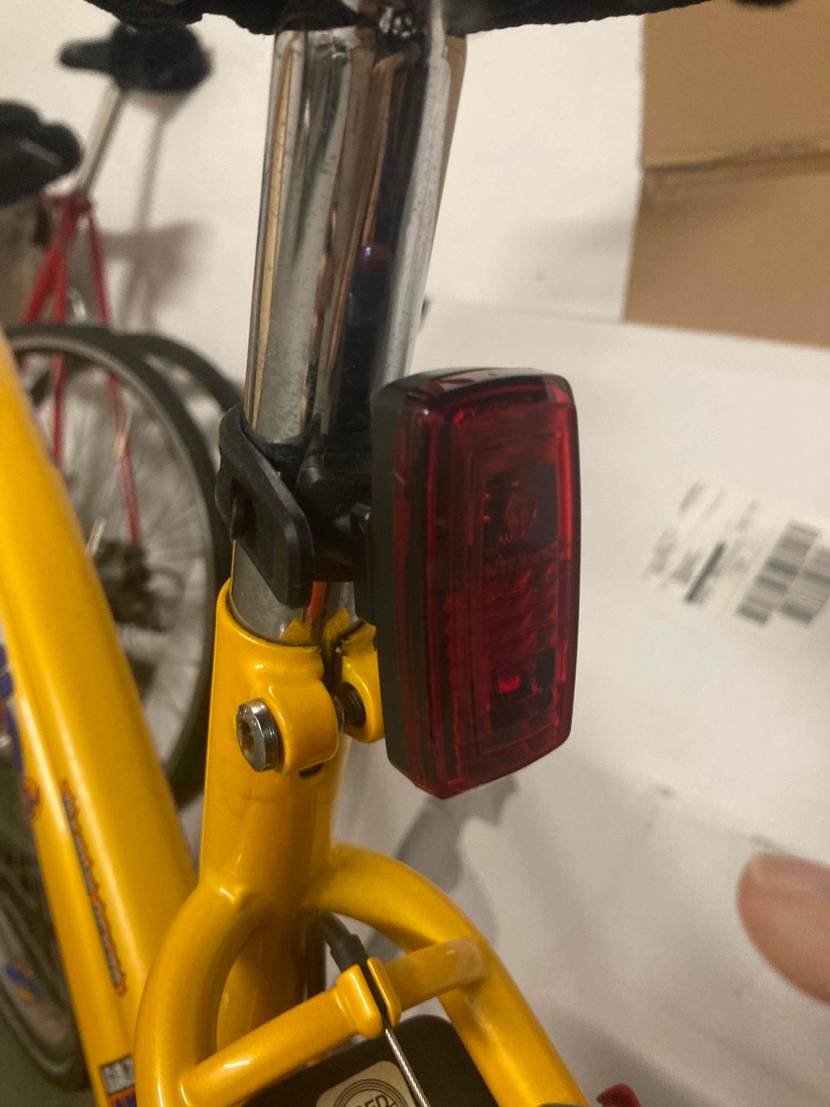 Rotes Rücklicht einer Fahrradbeleuchtung im Test befindet sich ausgeschaltet an einer Sattelstange eines gelben Fahrrads.