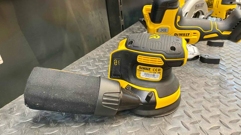 Exzenterschleifer-Test: Seitenansicht von einem gelb-schwarzen Schleifgerät der Marke DeWalt, inklusive Soft-Griff auf silberfarbener Metallfläche in einem Verkaufsbereich.