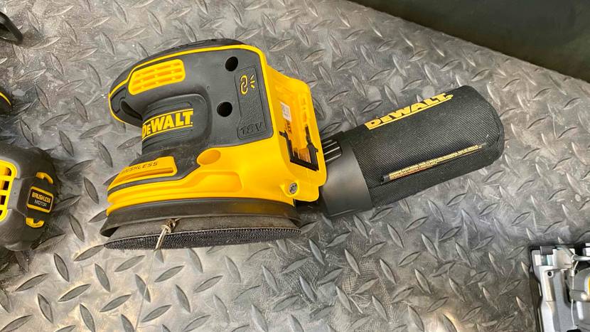 Exzenterschleifer im Test: Nahaufnahme von der Seite auf ein gelb-schwarzes Schleifgerät der Marke DeWalt, inklusive Soft-Griff und Kletterverschlusssystem auf silberfarbener Metallfläche.
