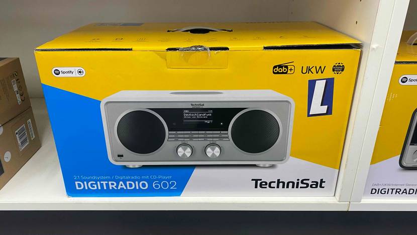Ein originalverpacktes Digitalradio von vorne in einem weißen Regal.