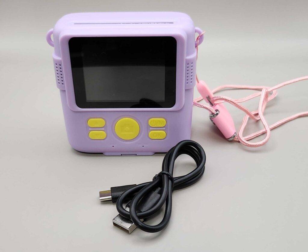 Getestet: Kinderkameras: Ein lila Modell steht neben einem rosa Fernauslöser und einem schwarzen USB-Kabel auf einer weißen Fläche.