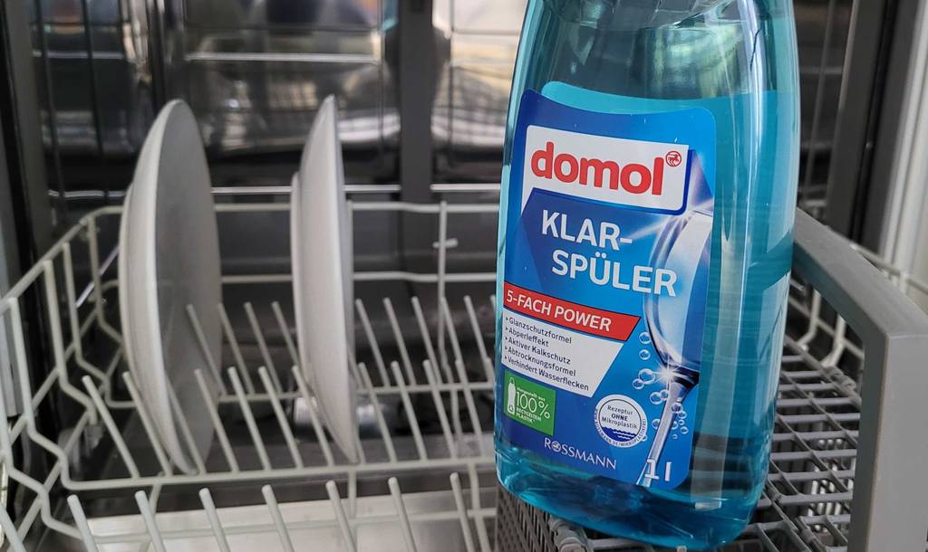 Domol Klarspüler steht auf einer geöffneten Spülmaschine mit Teller darin