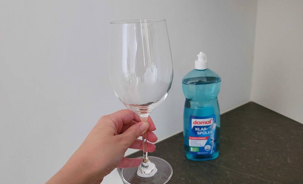 Hand hält ein sauberes Glas in der Hand, im Hintergrund Domol Klarspüler.