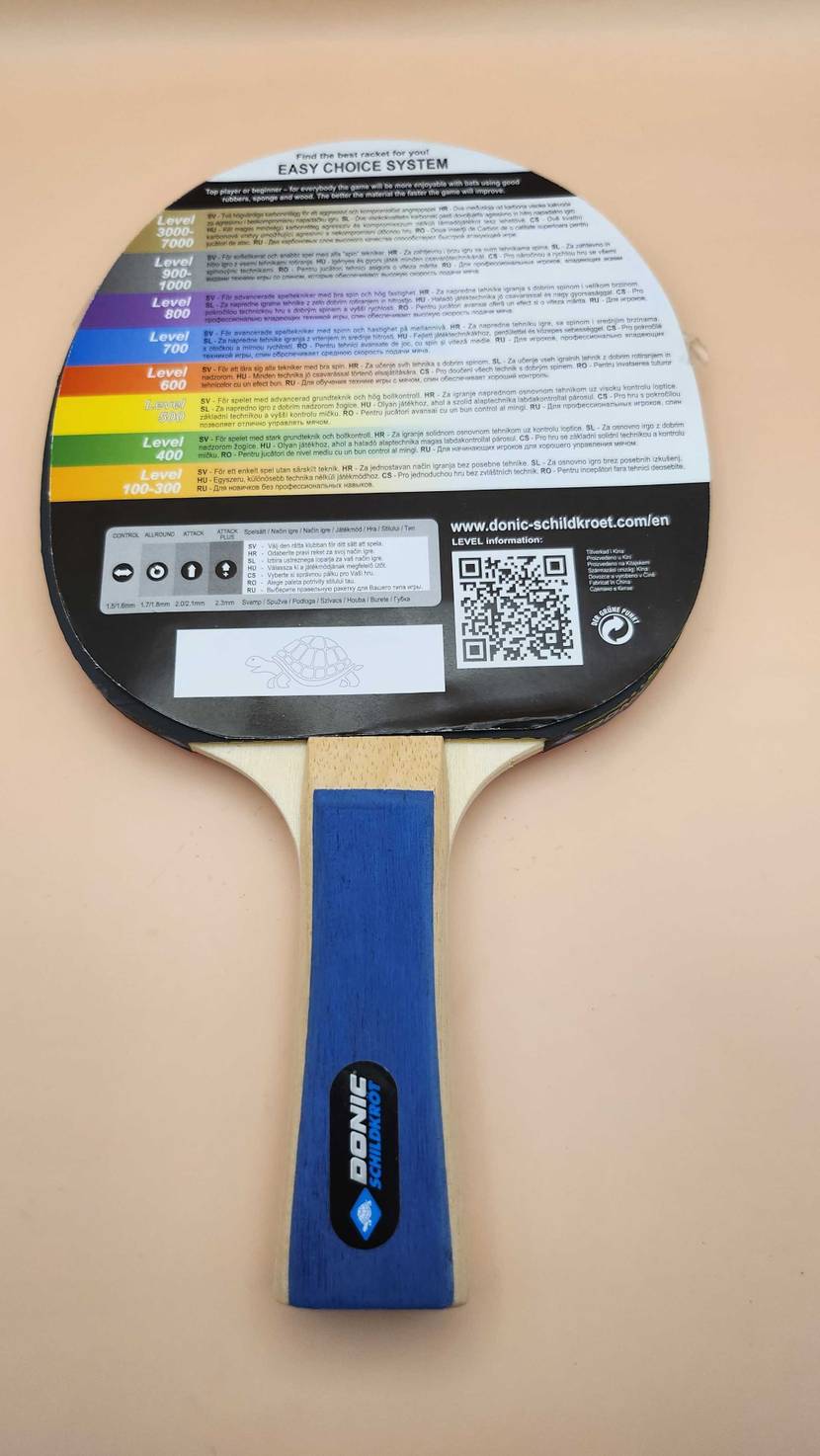 Der Tischtennisschläger im Test liegt inklusive Papierabdeckung mit Produktbeschreibung auf einer beigefarbenen Oberfläche.