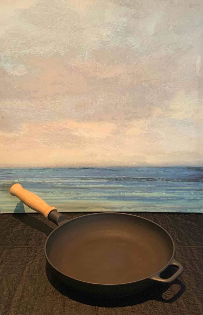 Vor einem Bild mit dem Meer steht auf einer dunklen Fläche die getestete Eisenpfanne.