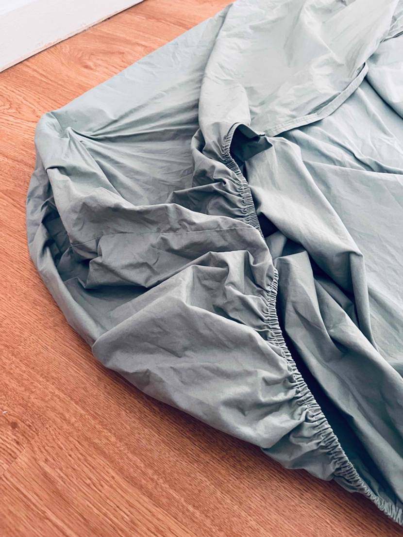 Elastischer Eckbereich eines hellgrauen getesteten Spannbettlakens auf Holzboden.