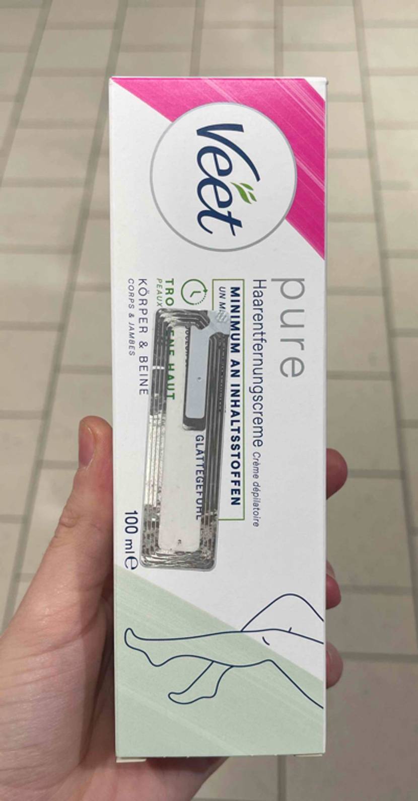Enthaarungsmittel-Test: Eine Hand hält eine Packung über einem Fliesenboden.
