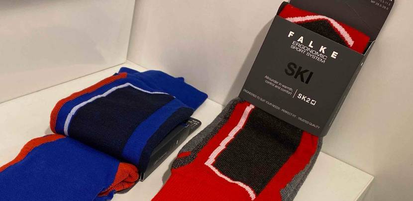 Zwei Paar Falke Skisocken im Test in der Grundfarbe Blau und Rot liegen auf einem weißen Regal.