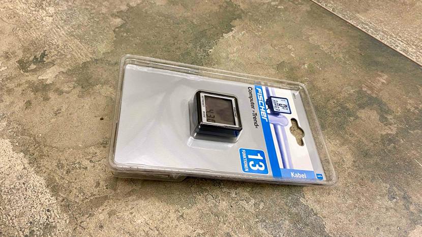 Ein verpackter Fahrradcomputer im Test auf einer grauen Fläche liegend.