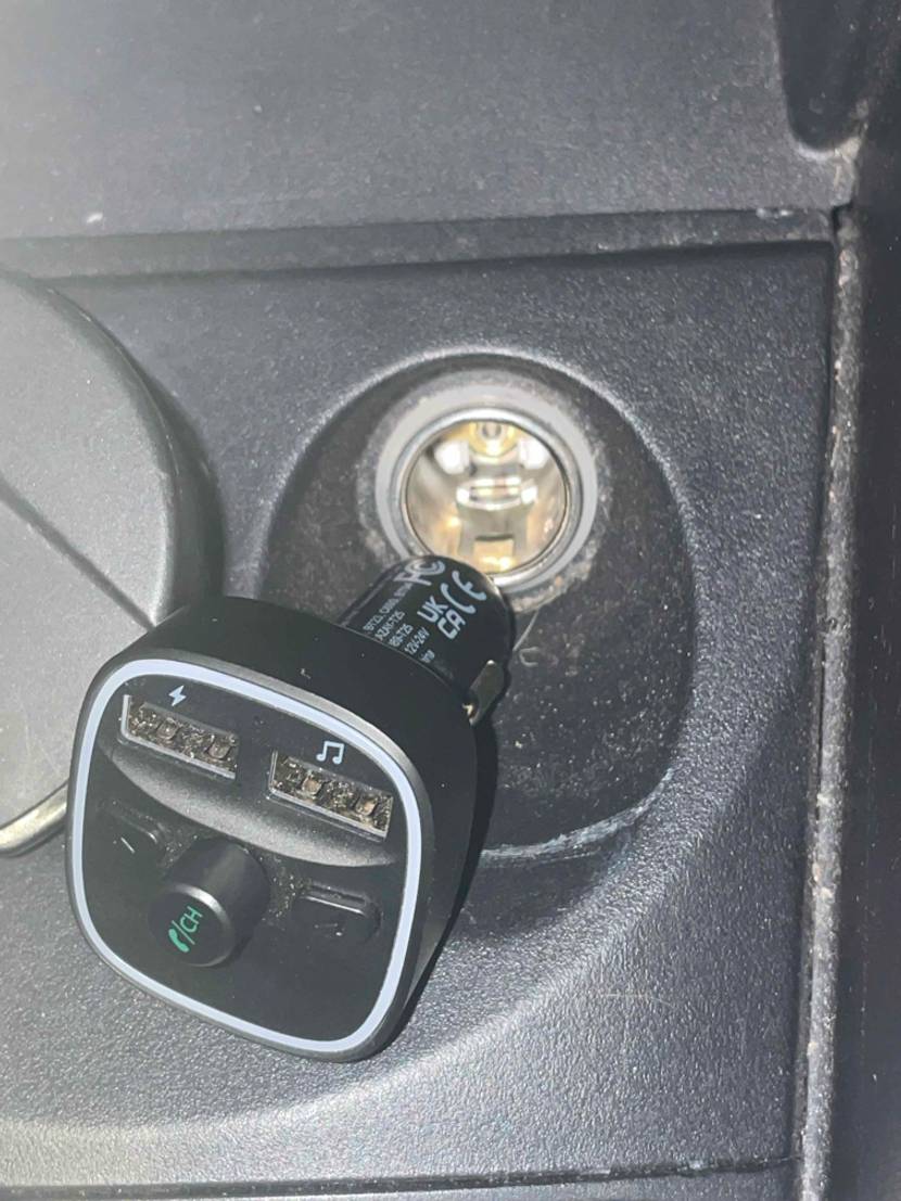 Ein schwarzer, getesteter FM-Transmitter inklusive Adapter befindet sich vor einem Zigarettenanzünder-Eingang im Fahrzeug.