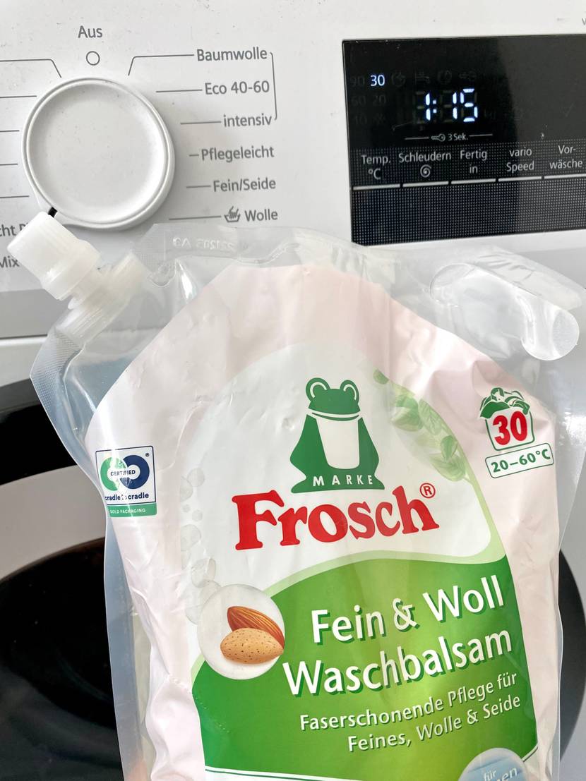 Flüssiges Waschmittel von Frosch vor einer Waschmaschine.