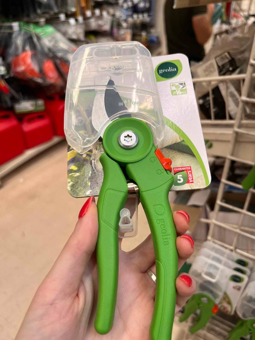 Eine Hand hält eine Gartenschere im Test vor ein Regal.